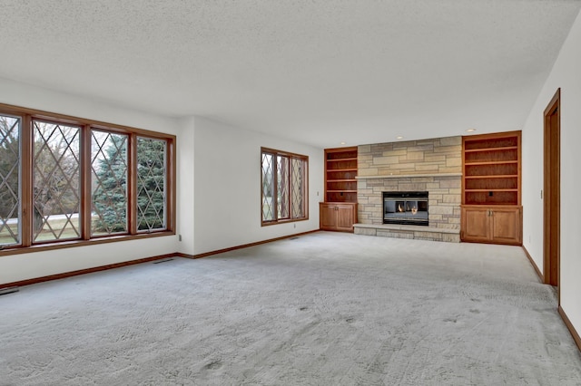 unfurnished living room featuring built in features, a textured ceiling, carpet floors, a fireplace, and baseboards