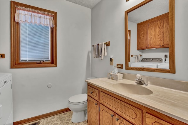 bathroom with baseboards, toilet, vanity, a textured ceiling, and separate washer and dryer