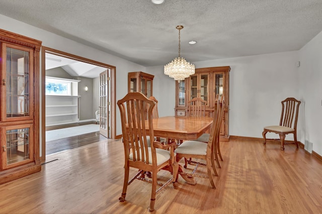 dining area with a chandelier, a textured ceiling, light wood-type flooring, and baseboards