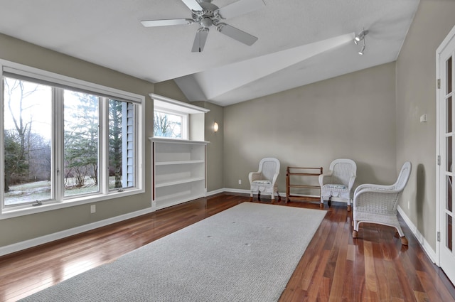 living area with baseboards, lofted ceiling, hardwood / wood-style floors, and a ceiling fan