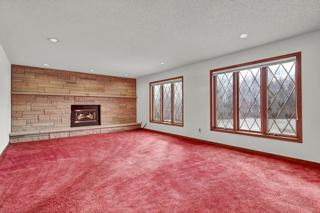 unfurnished living room featuring baseboards, a textured ceiling, a stone fireplace, and carpet flooring