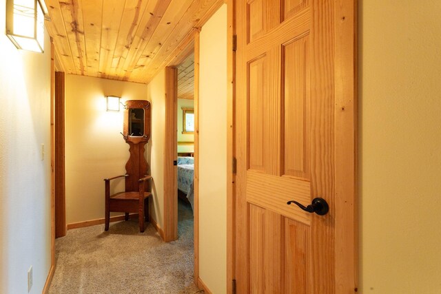 hallway featuring wooden ceiling, baseboards, and light carpet