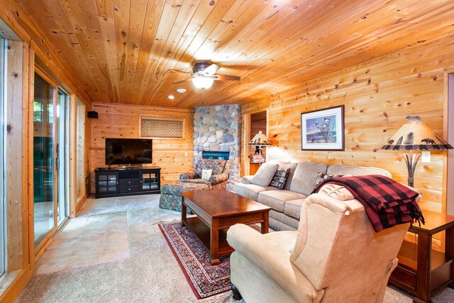 living area with a ceiling fan, carpet, a stone fireplace, wood ceiling, and wood walls