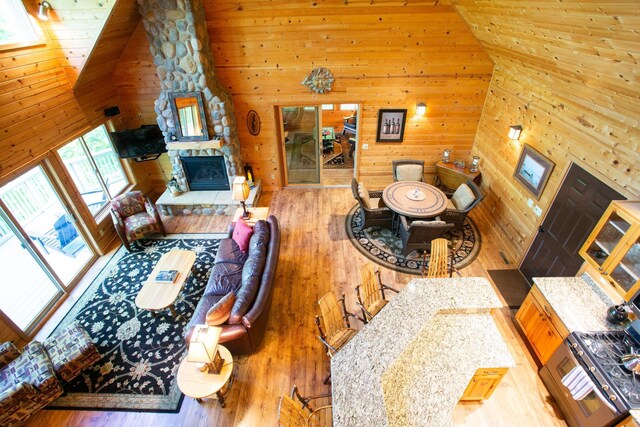 living room featuring wooden walls, high vaulted ceiling, a stone fireplace, hardwood / wood-style flooring, and wood ceiling