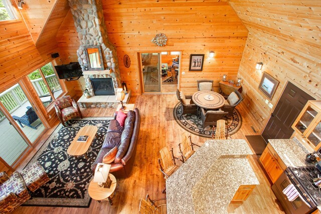 living area with wooden walls, a fireplace, high vaulted ceiling, and wood finished floors