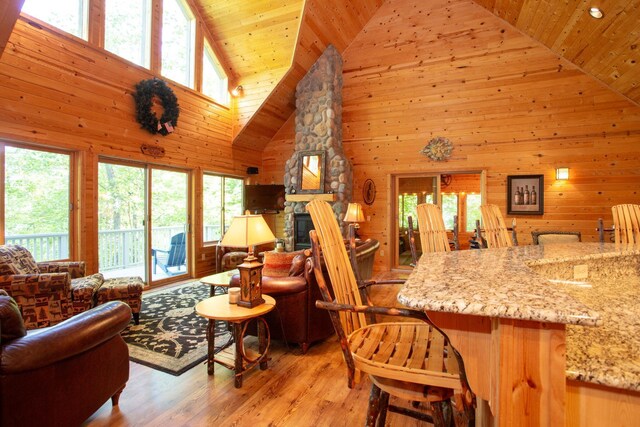 living area with a stone fireplace, wooden ceiling, light wood-style floors, and wood walls