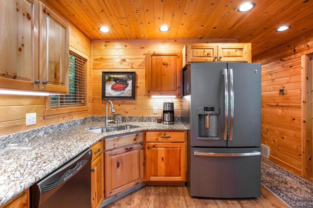 kitchen with wood walls, black dishwasher, wooden ceiling, stainless steel fridge, and a sink