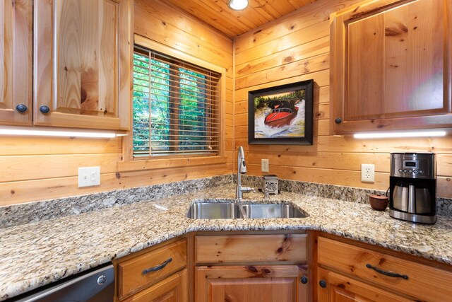 kitchen with a sink, light stone countertops, wooden walls, and dishwasher