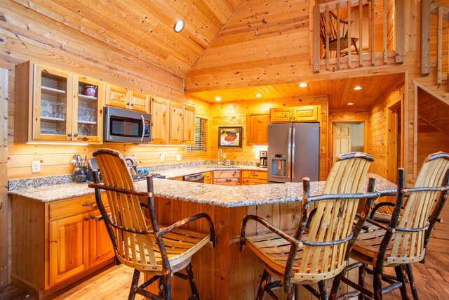 kitchen featuring wood walls, light wood-style flooring, appliances with stainless steel finishes, a kitchen breakfast bar, and a sink