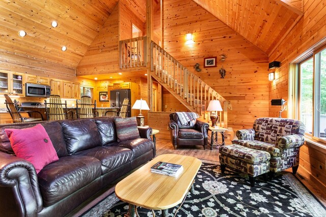 living area with stairway, wood walls, wood ceiling, wood finished floors, and high vaulted ceiling