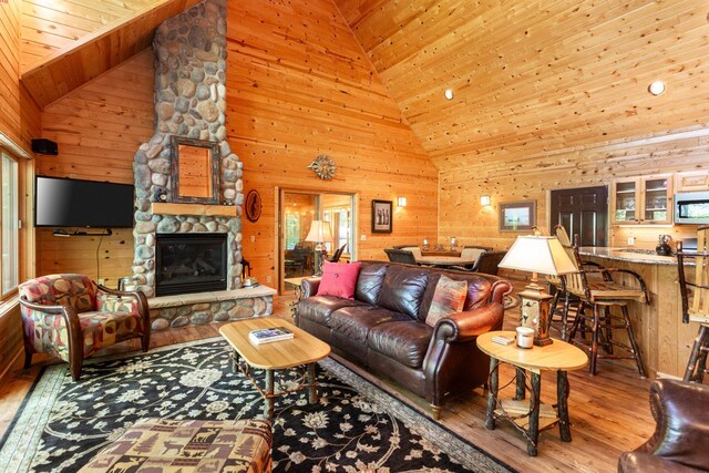 living area with a stone fireplace, wooden walls, wood finished floors, and wood ceiling