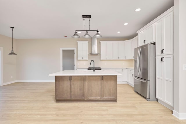 kitchen featuring a center island with sink, stainless steel fridge, wall chimney range hood, and white cabinetry