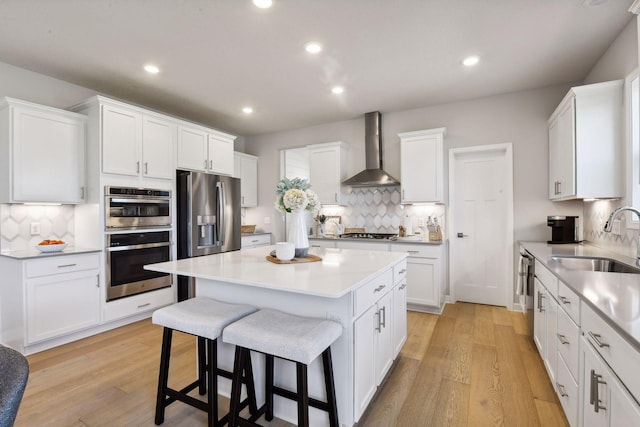 kitchen featuring wall chimney exhaust hood, stainless steel appliances, white cabinets, a center island, and sink