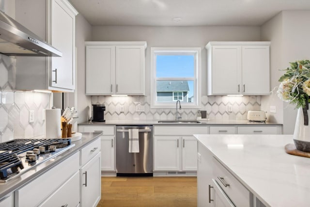 kitchen with white cabinetry, sink, stainless steel appliances, and wall chimney exhaust hood