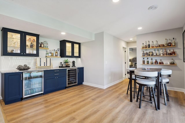 bar with wine cooler, light wood-type flooring, blue cabinets, and tasteful backsplash