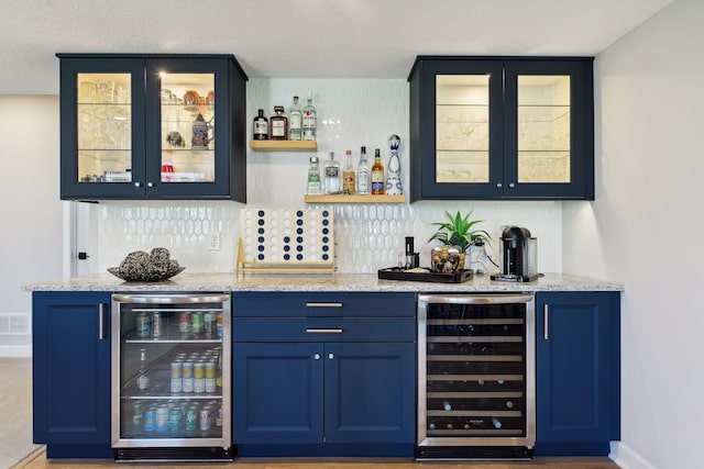 bar featuring blue cabinetry, beverage cooler, decorative backsplash, and light stone counters