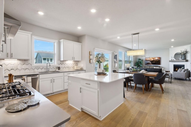 kitchen with a lit fireplace, a sink, light wood-style floors, backsplash, and a center island