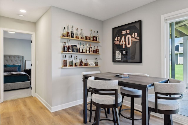 bar with a bar, baseboards, light wood-type flooring, and a healthy amount of sunlight