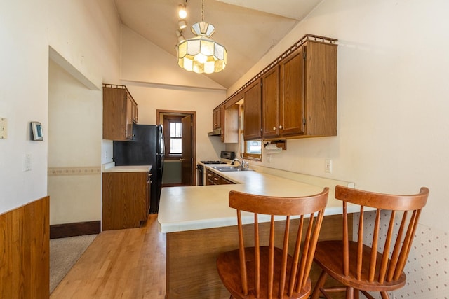 kitchen featuring sink, kitchen peninsula, vaulted ceiling, white range with gas stovetop, and a kitchen bar