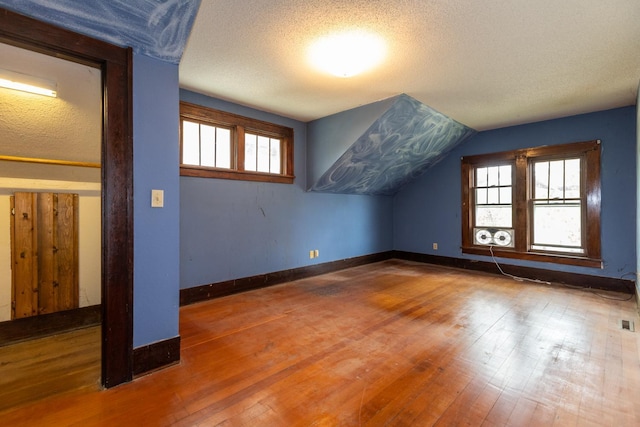 additional living space with a textured ceiling, a healthy amount of sunlight, lofted ceiling, and wood-type flooring