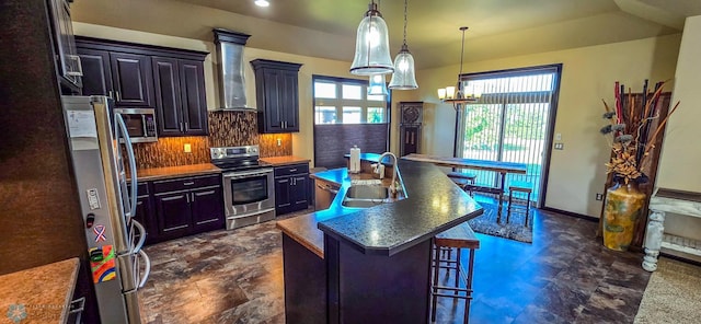 kitchen with wall chimney exhaust hood, stainless steel appliances, a kitchen bar, a center island with sink, and sink