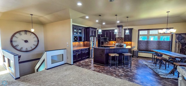 kitchen with an island with sink, appliances with stainless steel finishes, an inviting chandelier, vaulted ceiling, and decorative backsplash