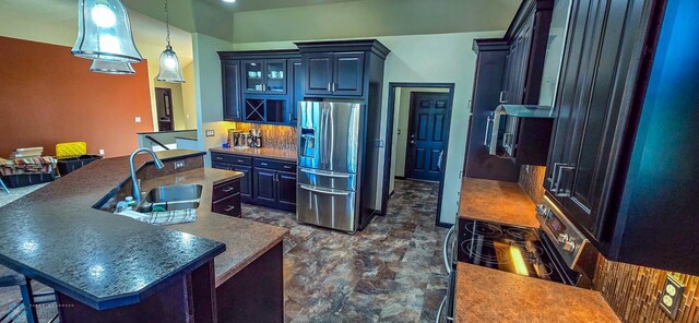 kitchen featuring pendant lighting, a kitchen island with sink, stainless steel fridge with ice dispenser, sink, and decorative backsplash