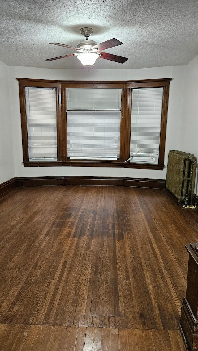 empty room featuring a textured ceiling, radiator, ceiling fan, and dark wood-type flooring