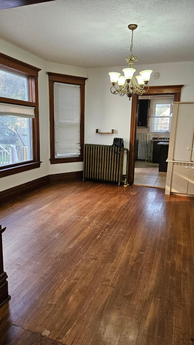 unfurnished dining area featuring a textured ceiling, wood-type flooring, radiator, and a notable chandelier