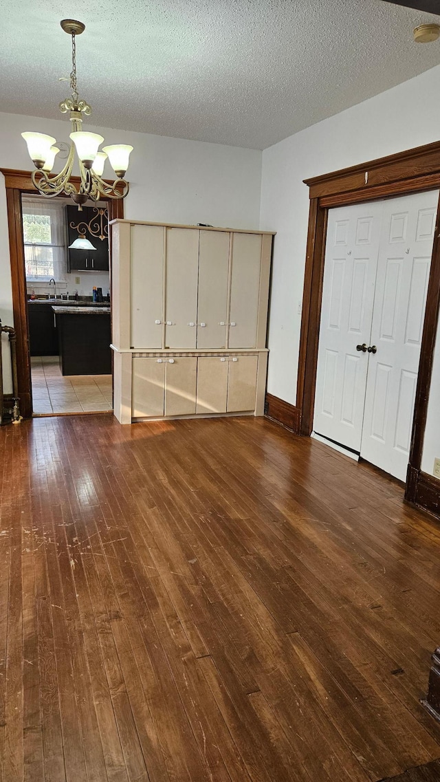 unfurnished bedroom featuring a notable chandelier, a textured ceiling, and dark hardwood / wood-style flooring