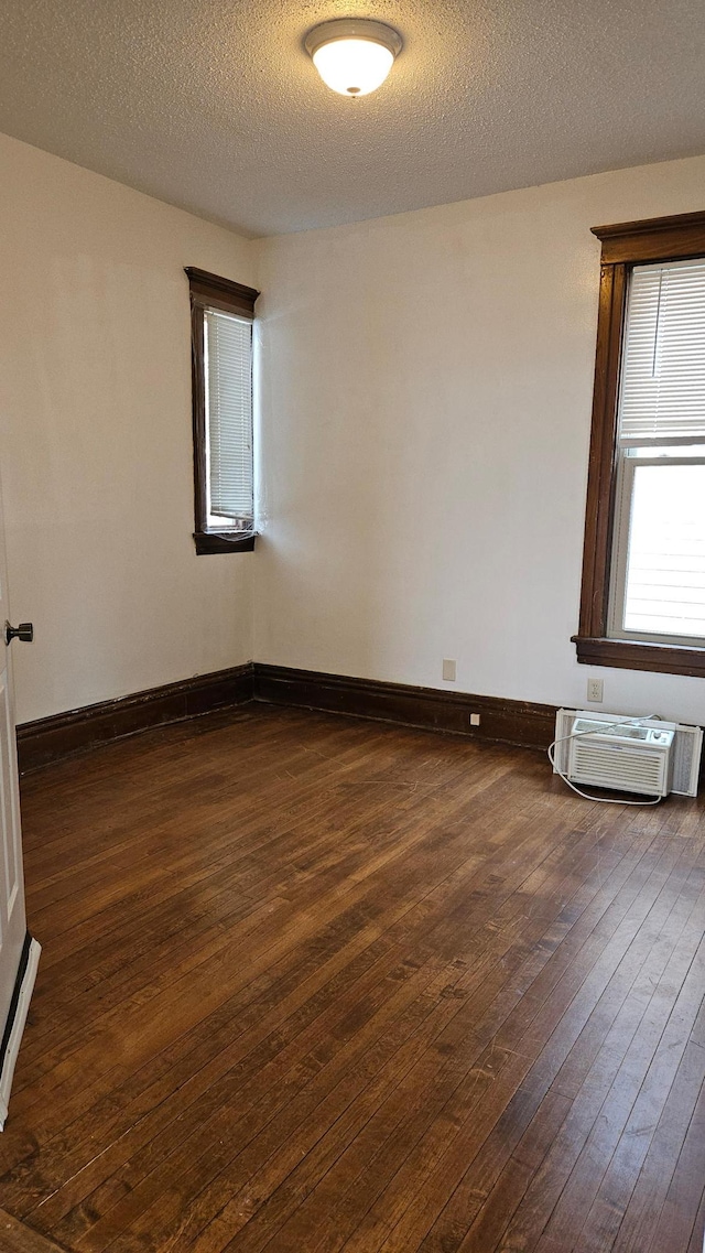 empty room featuring a textured ceiling, dark wood-type flooring, and a wall mounted AC