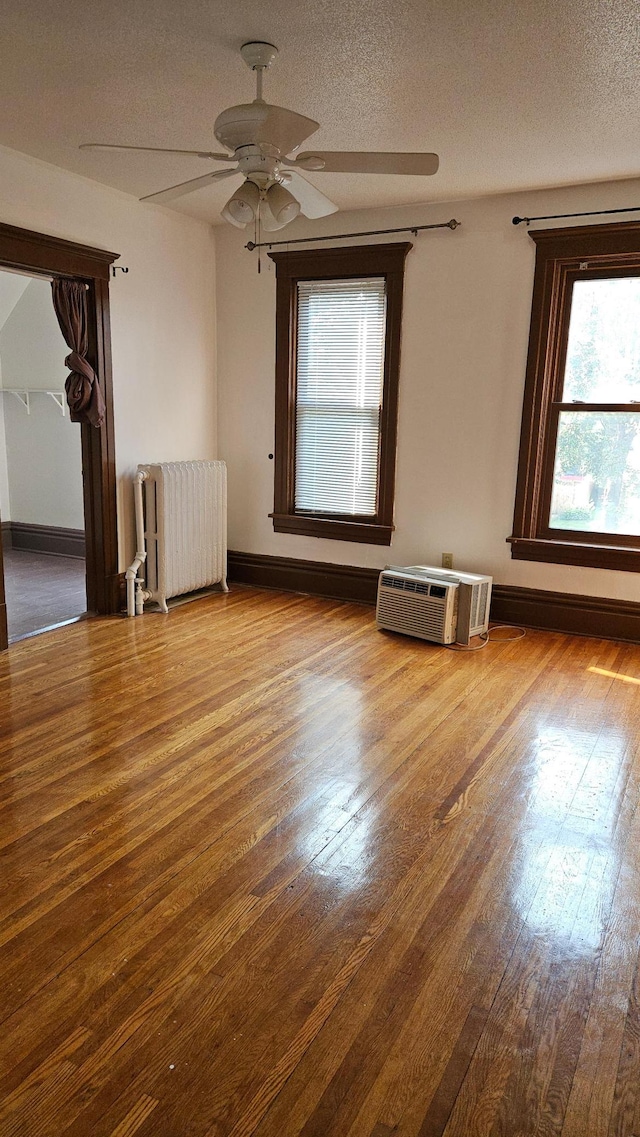 empty room featuring a textured ceiling, wood-type flooring, radiator, ceiling fan, and a wall mounted AC