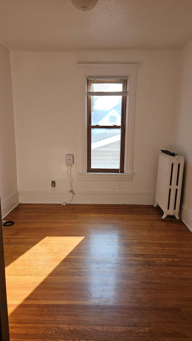 spare room with radiator, a textured ceiling, and dark wood-type flooring