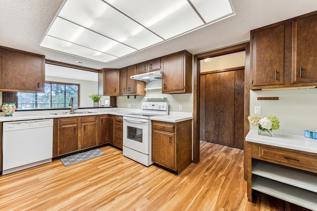 kitchen with a textured ceiling, white appliances, sink, and light hardwood / wood-style flooring