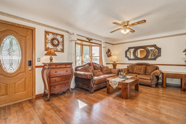 living room with light hardwood / wood-style flooring, ceiling fan, ornamental molding, and a textured ceiling