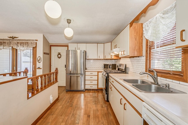 kitchen with hanging light fixtures, sink, white cabinetry, stainless steel appliances, and light wood-type flooring