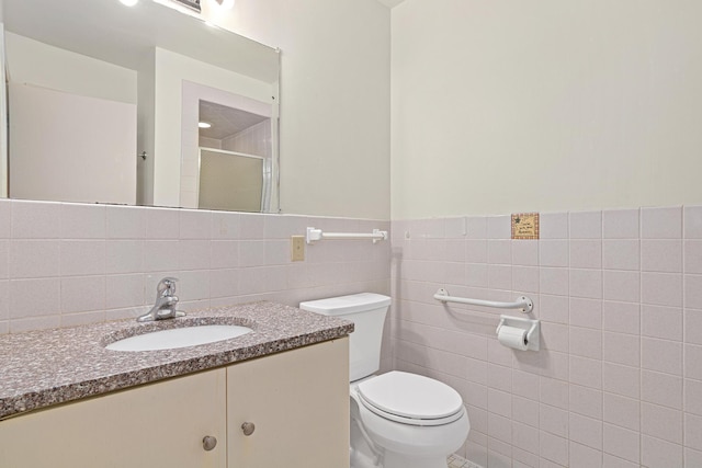 bathroom with vanity, toilet, tile walls, and a shower with door