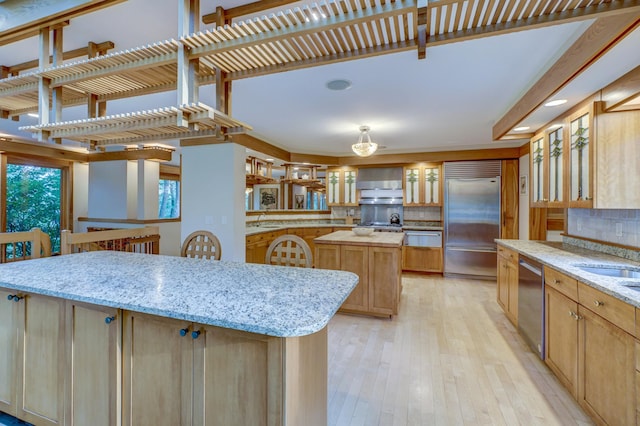 kitchen featuring stainless steel appliances, a center island, light stone countertops, light hardwood / wood-style floors, and decorative backsplash