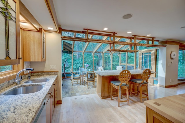 kitchen featuring light stone countertops, light hardwood / wood-style flooring, sink, and a breakfast bar