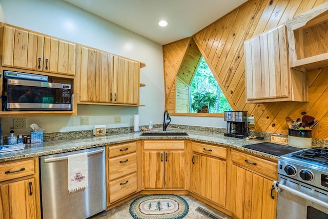 kitchen featuring light stone countertops, wooden walls, sink, and stainless steel appliances