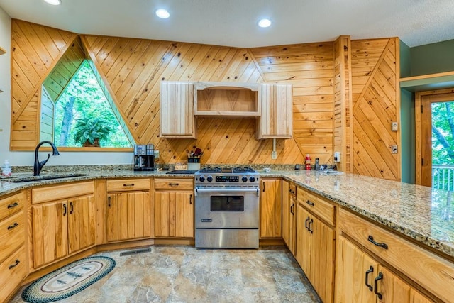 kitchen with wooden walls, light stone counters, high end stove, and sink