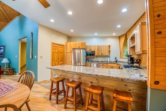 kitchen with light stone counters, sink, kitchen peninsula, stainless steel appliances, and light hardwood / wood-style floors