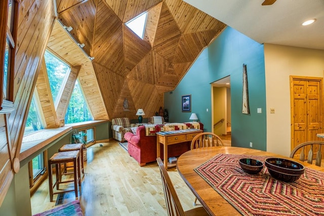 dining area with a skylight, light wood-type flooring, wood walls, and high vaulted ceiling