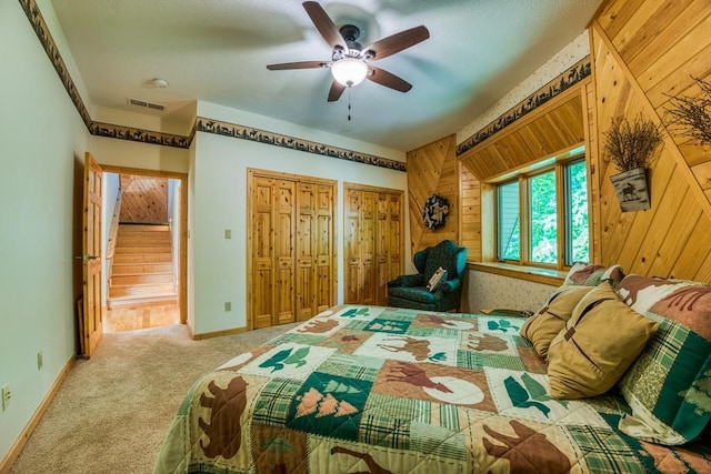 bedroom featuring ceiling fan, multiple closets, wooden walls, and light carpet