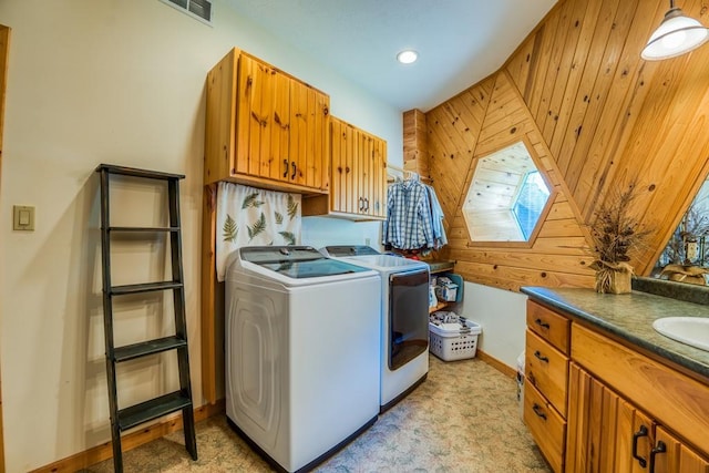 clothes washing area featuring cabinets, wooden walls, sink, and independent washer and dryer