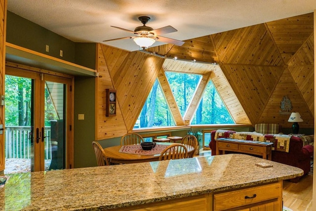 kitchen featuring lofted ceiling, wood walls, light hardwood / wood-style flooring, light stone countertops, and ceiling fan