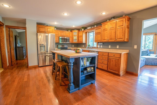 kitchen with light wood-type flooring, sink, a kitchen island, stainless steel appliances, and wooden counters