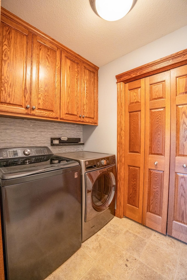 laundry area with a textured ceiling, light tile patterned floors, washing machine and clothes dryer, and cabinets