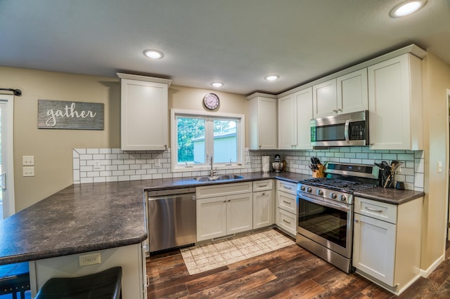 kitchen with appliances with stainless steel finishes, white cabinetry, kitchen peninsula, dark hardwood / wood-style flooring, and sink