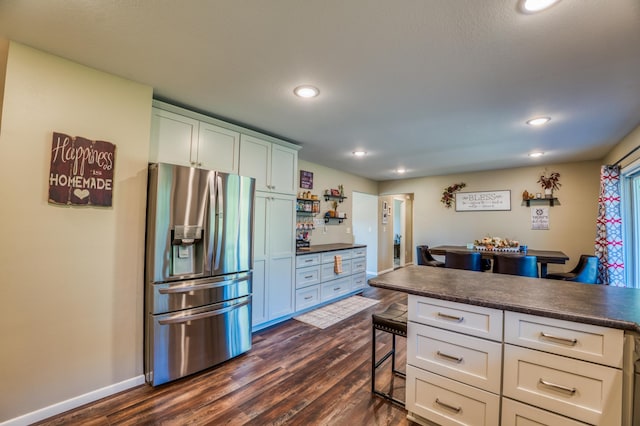 kitchen featuring stainless steel fridge, a kitchen bar, white cabinetry, and dark wood-type flooring